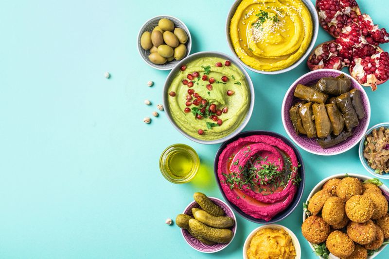 Arabic traditional cuisine. Middle Eastern meze with pita, olives, colorful hummus, falafel, stuffed dolma, babaganush, pickles, vegetables, pomegranate, eggplants. Mediterranean appetizer party idea.