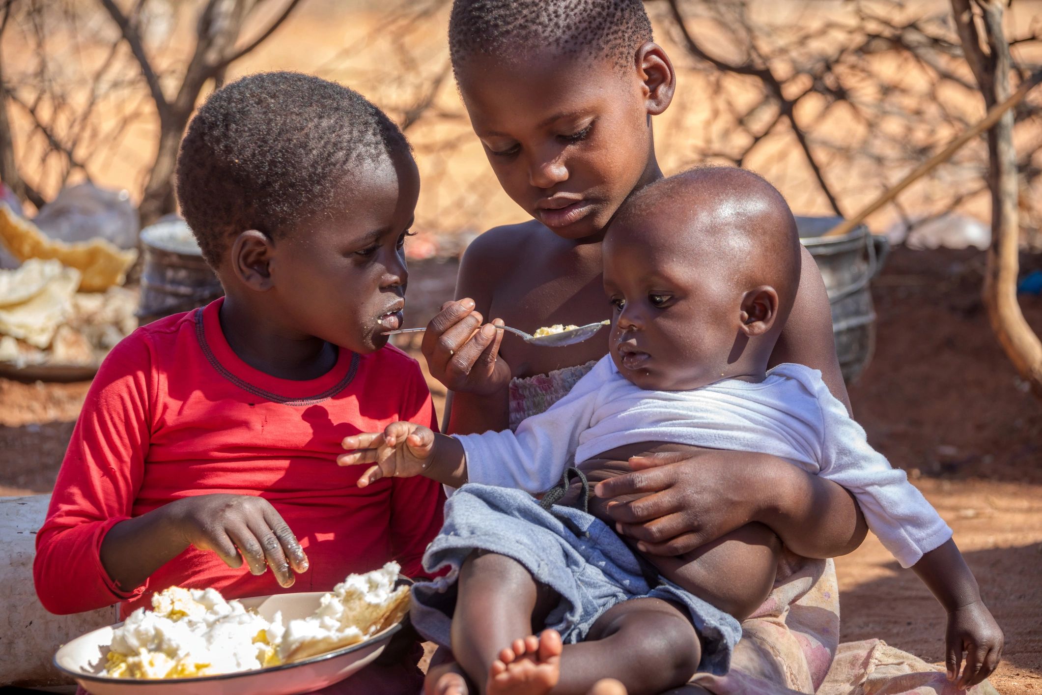 Three children sharing food outdoors.