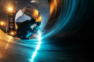 Welder working inside a large metal pipe.