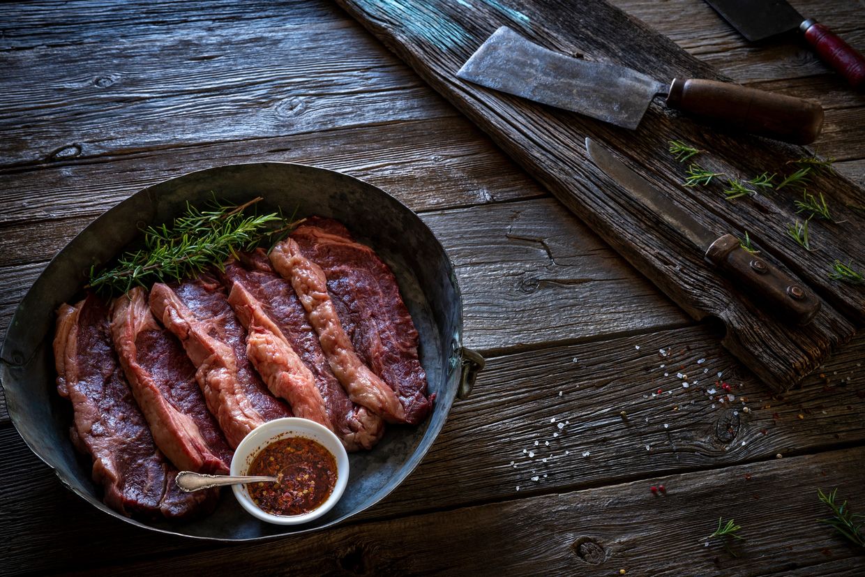 Raw beef steaks with herbs and sauce on rustic wooden table.
