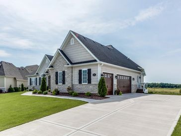 A beige and house in the middle of a large yard at the top of the driveway.