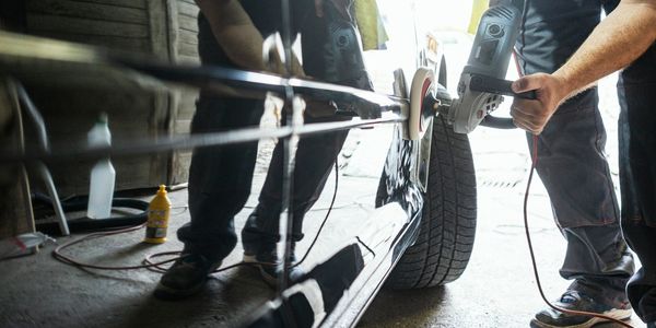 Person polishing a black car with a power buffer in a garage.