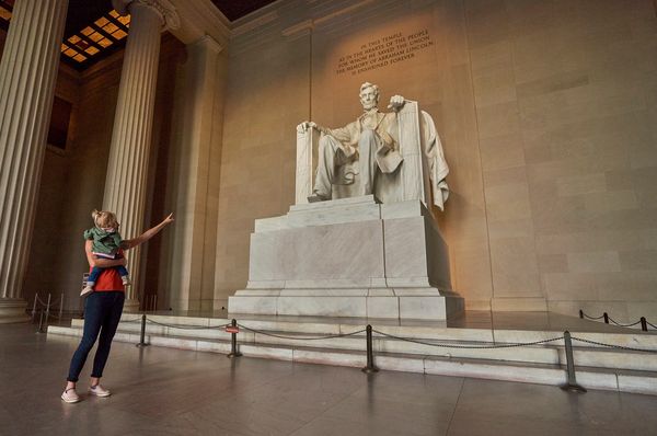 Person holding a child inside the Lincoln Memorial with the statue of Abraham Lincoln.