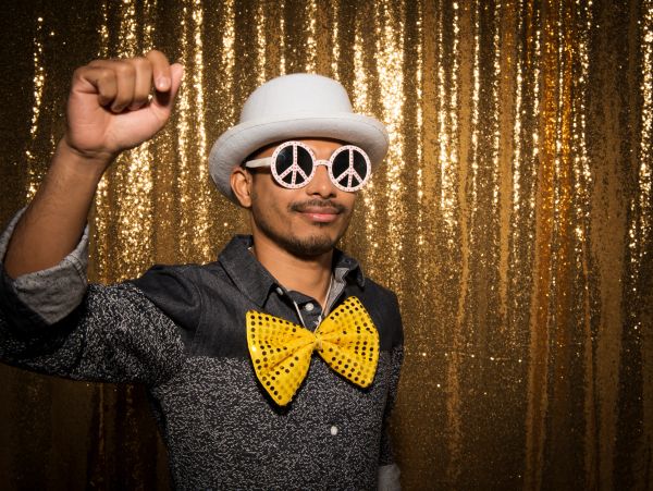 Happy woman with red lipstick holding mustache and glasses props against pink background.