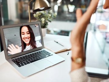 Woman waving during a video call on laptop.