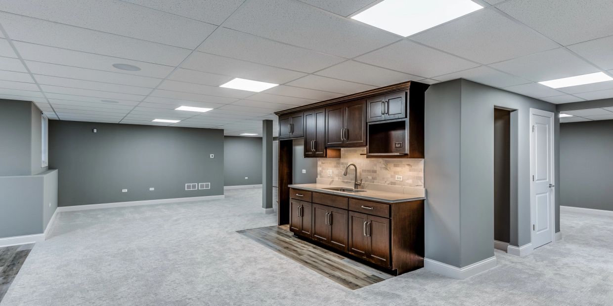 Spacious basement with gray walls and a kitchenette with dark wood cabinets.