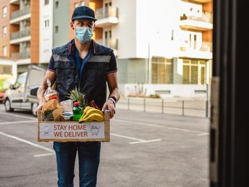 Delivery man with groceries wearing a mask outside an apartment building.