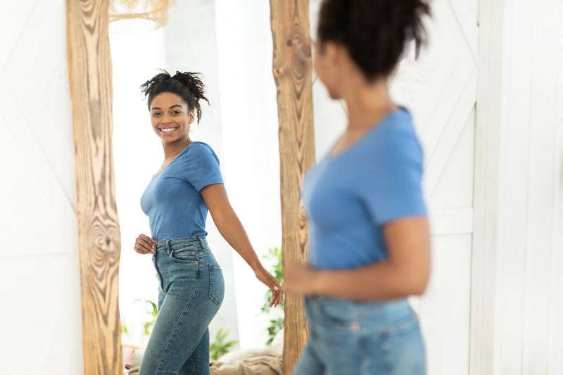 Successful Weight Loss. Joyful African American Girl After Slimming Smiling To Her Reflection In Mirror Standing At Home. Staying Fit, Dieting And Weight-Loss Concept. Selective Focus
