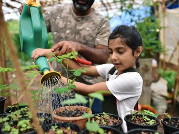 A man helps a young girl water plants in a greenhouse.