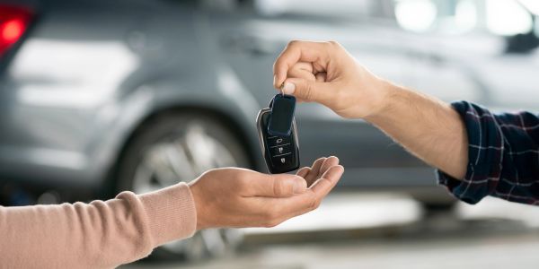 Person handing over a car key to another person.