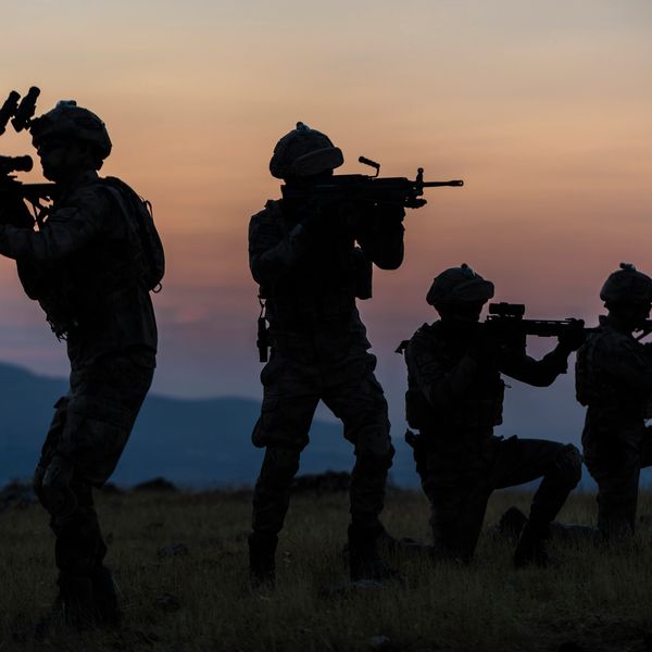 Silhouettes of soldiers aiming rifles at sunset.