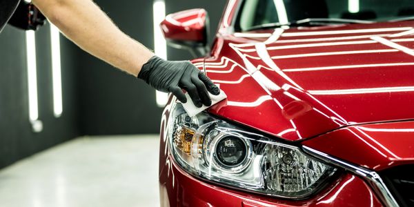 Person polishing the headlight area of a shiny red car.