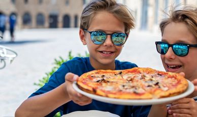 Two boys holding a delicious mushroom pizza outdoors.