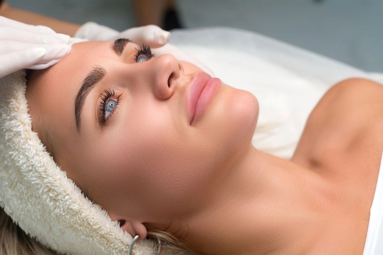 Woman receiving a facial treatment with a headband and gloves on.