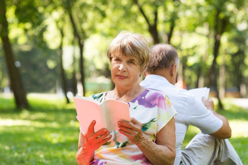senior couple read bookssitting on the grass in the park on a summer day