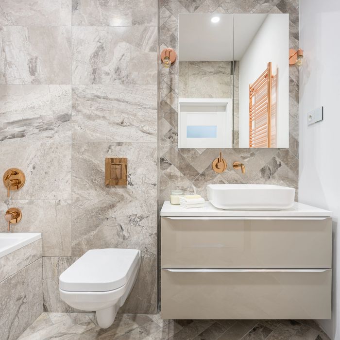 Modern bathroom with beige marble tiles and rose gold fixtures.