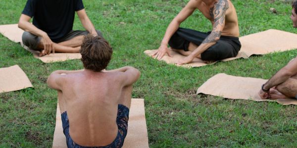 A group of people sitting on mats outdoors, engaged in a yoga or meditation session.