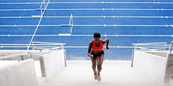 Athlete sprinting up stadium stairs with blue track in background.