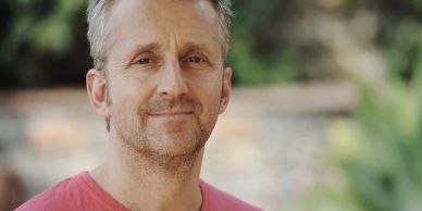 Man smiling outdoors in a red shirt.