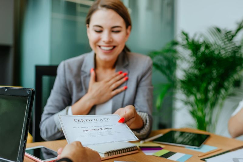 Happy smiling business woman receiving a certificate sitting at the table in office. Selective focus on the certificate.