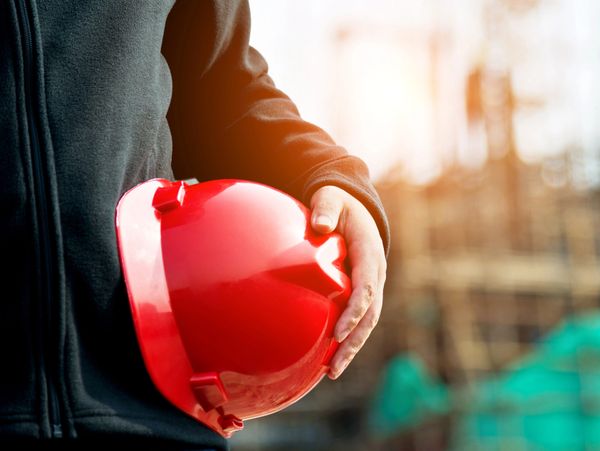 Person holding a red safety helmet at a construction site.