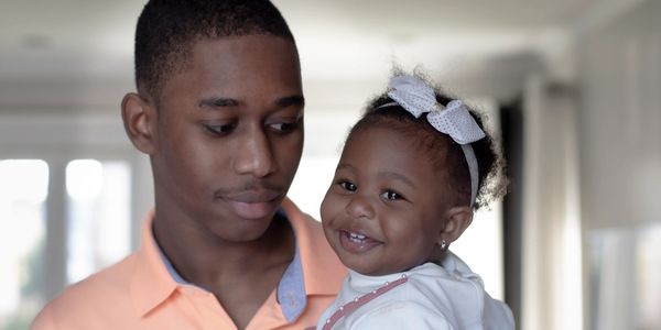 Young man holding smiling baby girl with bow.