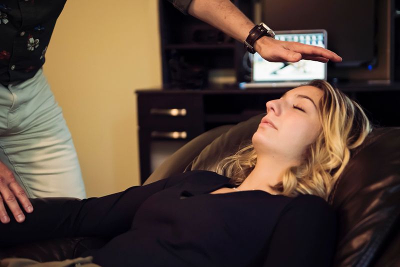 Young woman in hypnosis session with mature man hypnotherapist. Both are  wearing casual clothes. She is lying down for hypnotherapy session. Horizontal waist up indoors shot with copy space.