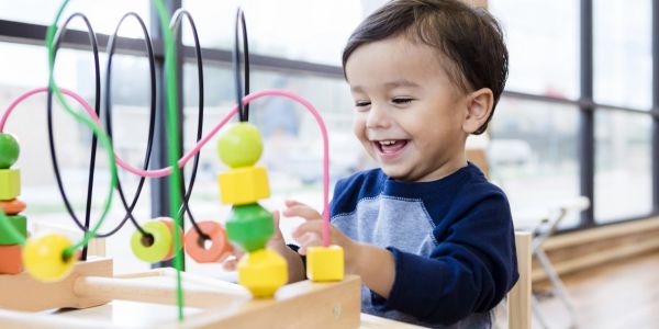 Happy toddler playing with colorful wooden bead maze toy.