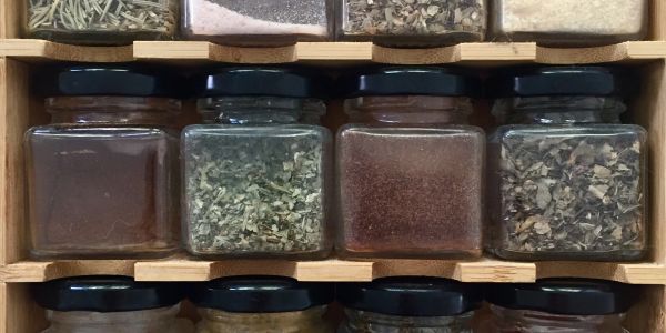 Glass jars of various spices in a wooden rack.