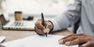 Person signing a document with a pen at a desk.