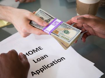 Hands exchanging cash over a home loan application document.