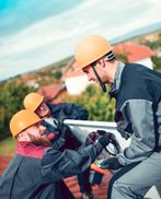 Two construction workers wearing helmets and protective gear interact on site.