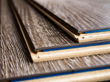 Stack of wooden laminate flooring panels with textured surfaces.