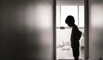 Silhouette of a child standing in a hallway with head bowed.