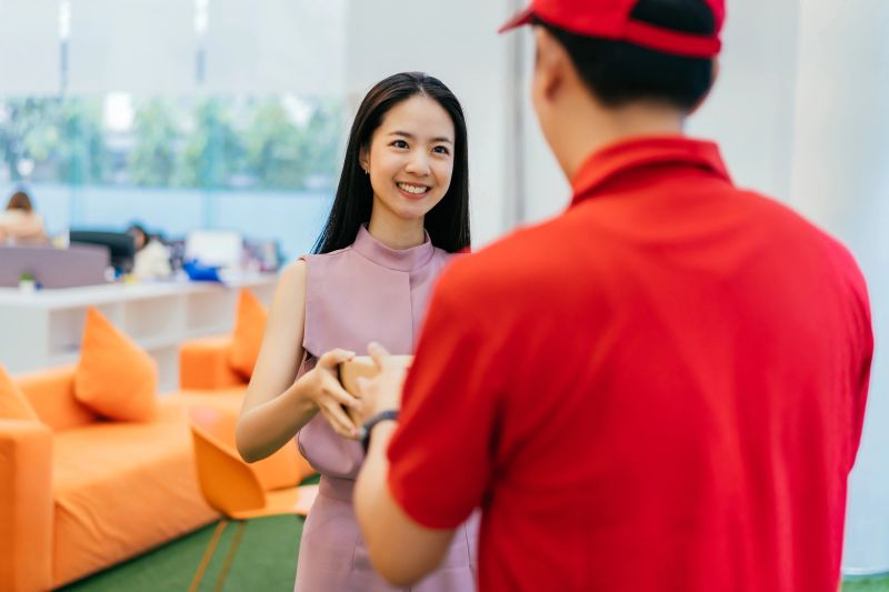 Happy Asian businesswoman taking pizza boxes from pizza delivery man, lunch break, takeaway pizza delivery, food and drink
