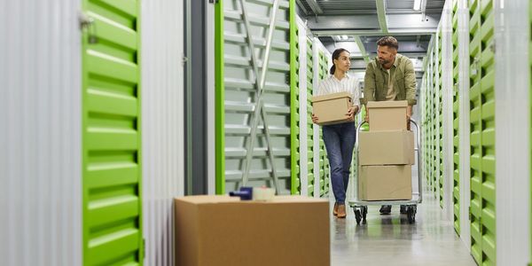 A couple moves boxes through a storage facility with green doors.