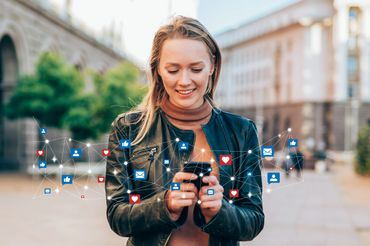 A woman using her phone with social media icons floating around.
