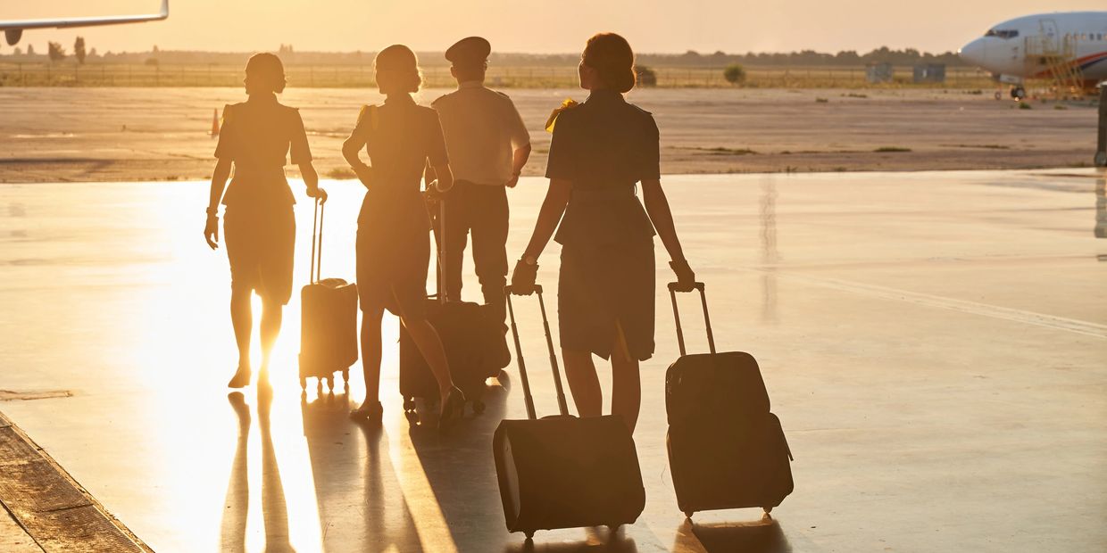 Flight crew walking on airport tarmac with luggage at sunset.