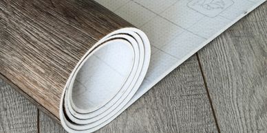 Rolled vinyl flooring with wood texture on a wooden floor.