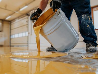 Person pouring yellow paint from a metal bucket.