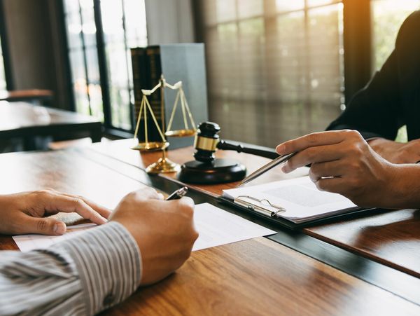 Two people meet at a wooden table, discussing documents with a gavel and scales of justice 