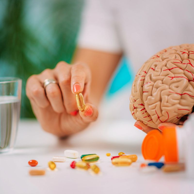 Cognitive improvement or brain supplements. Woman holding a supplement capsule and a model brain.