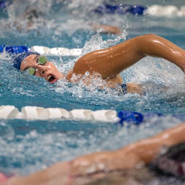 Swimmer in goggles competing in a freestyle race in a pool.