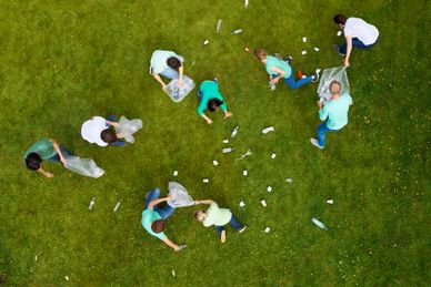 Group of people picking up litter in a grassy area with bags.