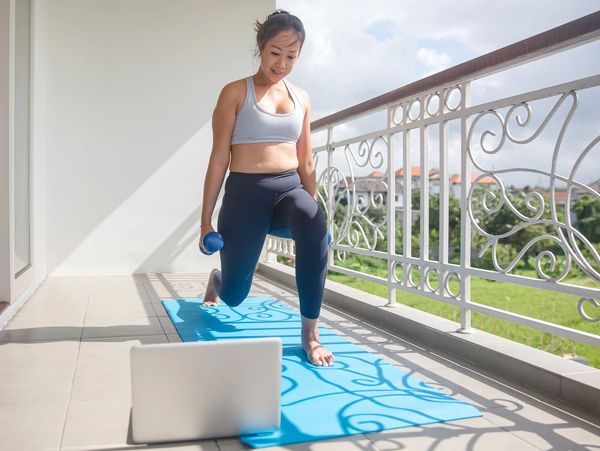 Woman exercising on balcony using laptop for workout guidance.