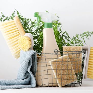 Basket with cleaning brushes, sponges, spray bottle, and cloth.
