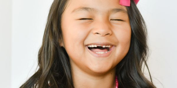 A joyful young girl laughing with missing front teeth, wearing a pink bow.