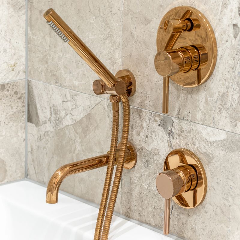 Close-up on architectural detail, golden bathtub faucet and shower handle in bathroom with marble tiles