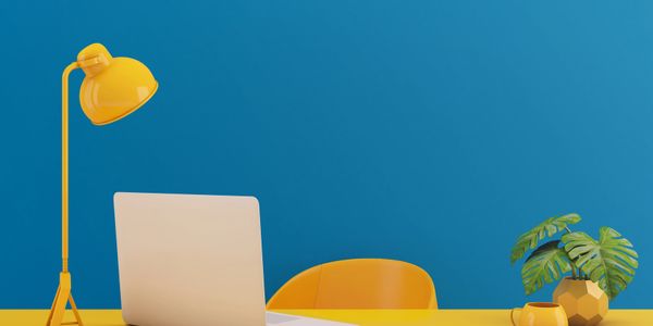 Bright yellow desk setup with laptop, lamp, cup, and plant against a blue wall.