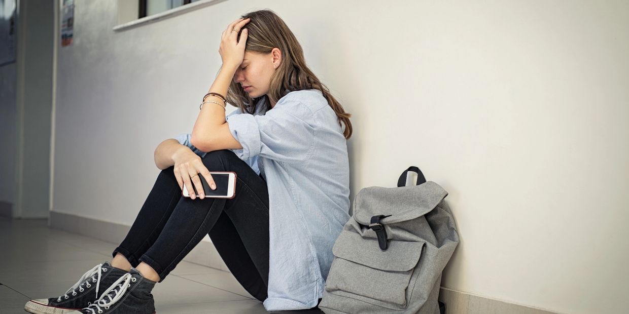 A stressed young woman sitting on the floor holding her phone, looking troubled.